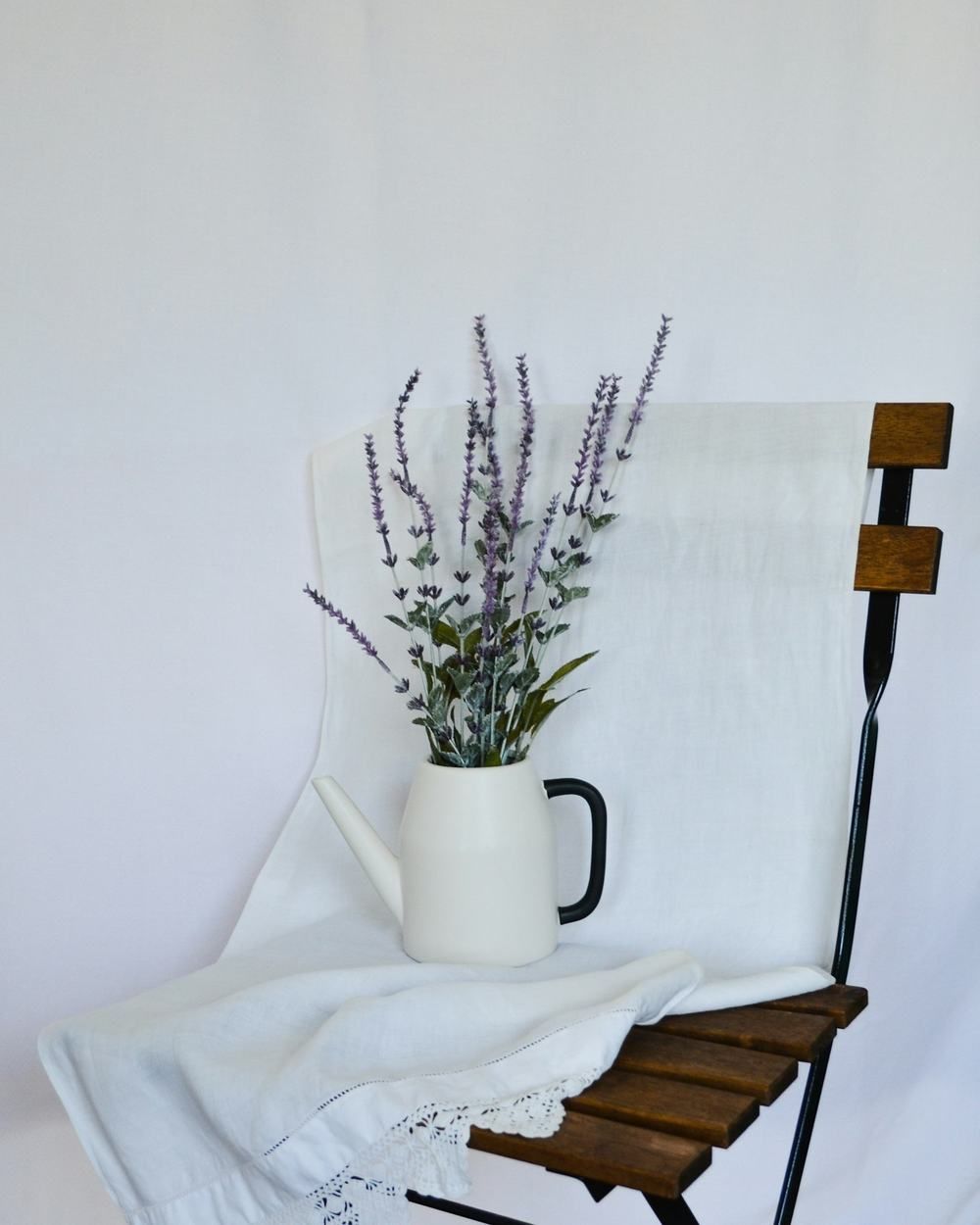 Bouquet de lavande dans un pichet blanc posé sur une chaise drapée de lin